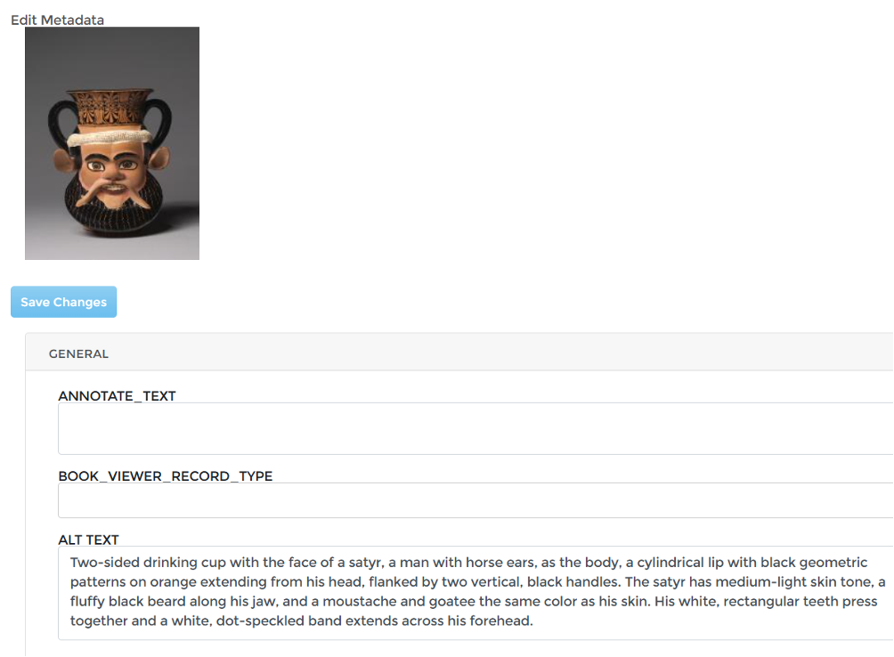 An "Edit Metadata" interface of a website. At the upper left is a preview image of a decorative two-sided drinking cup with black handles and a painted satyr-like face, including large eyes, ears, facial hair, and an ornate cylindrical top. Beneath the preview is a blue "Save Changes" button. The lower portion contains a "GENERAL" metadata section with empty fields labeled "ANNOTATE_TEXT" and "BOOK_VIEWER_RECORD_TYPE," followed by an "ALT TEXT" field filled with a detailed description of the cup's appearance, "Two-sided drinking cup with the face of a satyr, a man with horse ears, as the body, a cylindrical lip with black geometric patterns on orange extending from his head, flanked by two vertical, black handles. The satyr has medium-light skin tone, a fluffy black beard along his jaw, and a moustache and goatee the same color as his skin. His white, rectangular teeth press together and a white, dot-speckled band extends across his forehead."