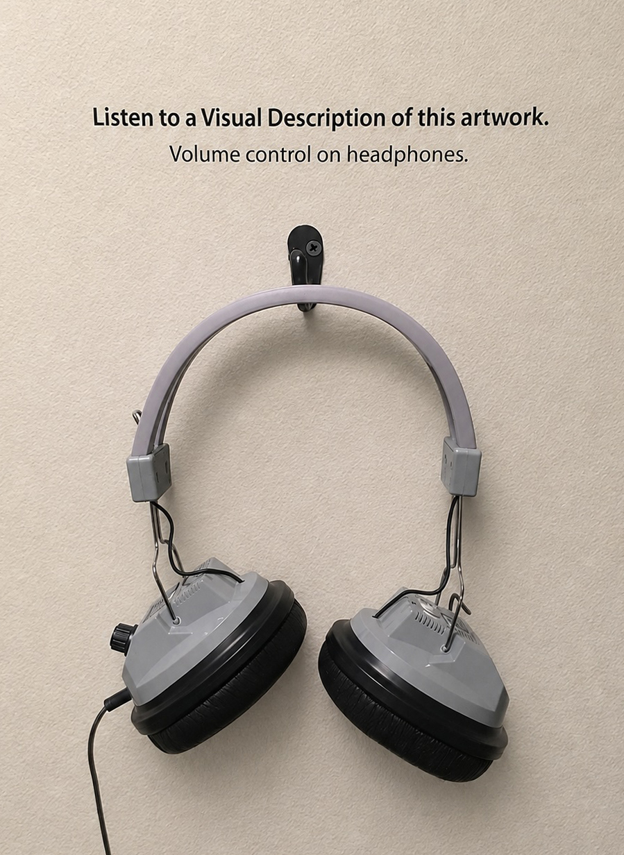 Gray over-ear headphones hanging from a small black wall hook on a lightly textured beige wall. Centered above the headphones, black printed text reads: Listen to a Visual Description of this artwork. Below it, a second centered line reads: Volume control on headphones. The headphones have a pale gray arched headband, silver wire supports, gray plastic earcup housings, and black padded ear cushions. The earcups hang open, with the left earcup angled slightly lower and outward. A small black volume knob is visible on the outside of the left earcup, and a black cable extends from that side downward out of the bottom of the image. The black hook is mounted above the headband with a visible screw near its top.